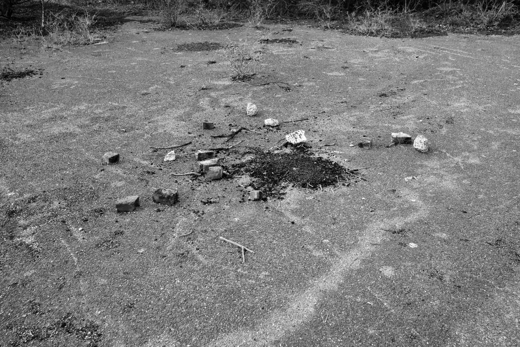 A small burnt circle of ash and bricks on the concrete apron, arranged as a rough firepit.