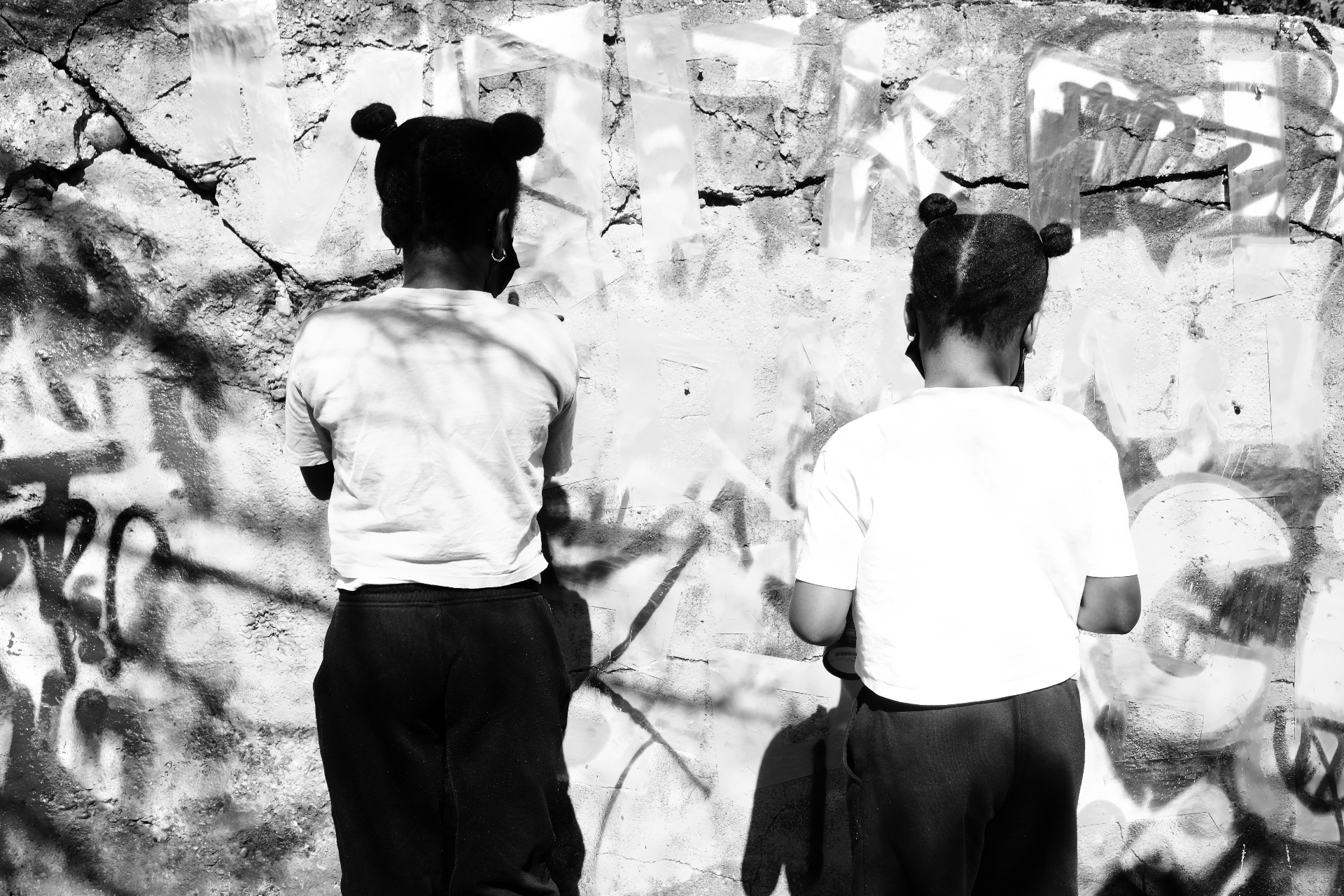 Two girls painting over taped-off letters on the wall.