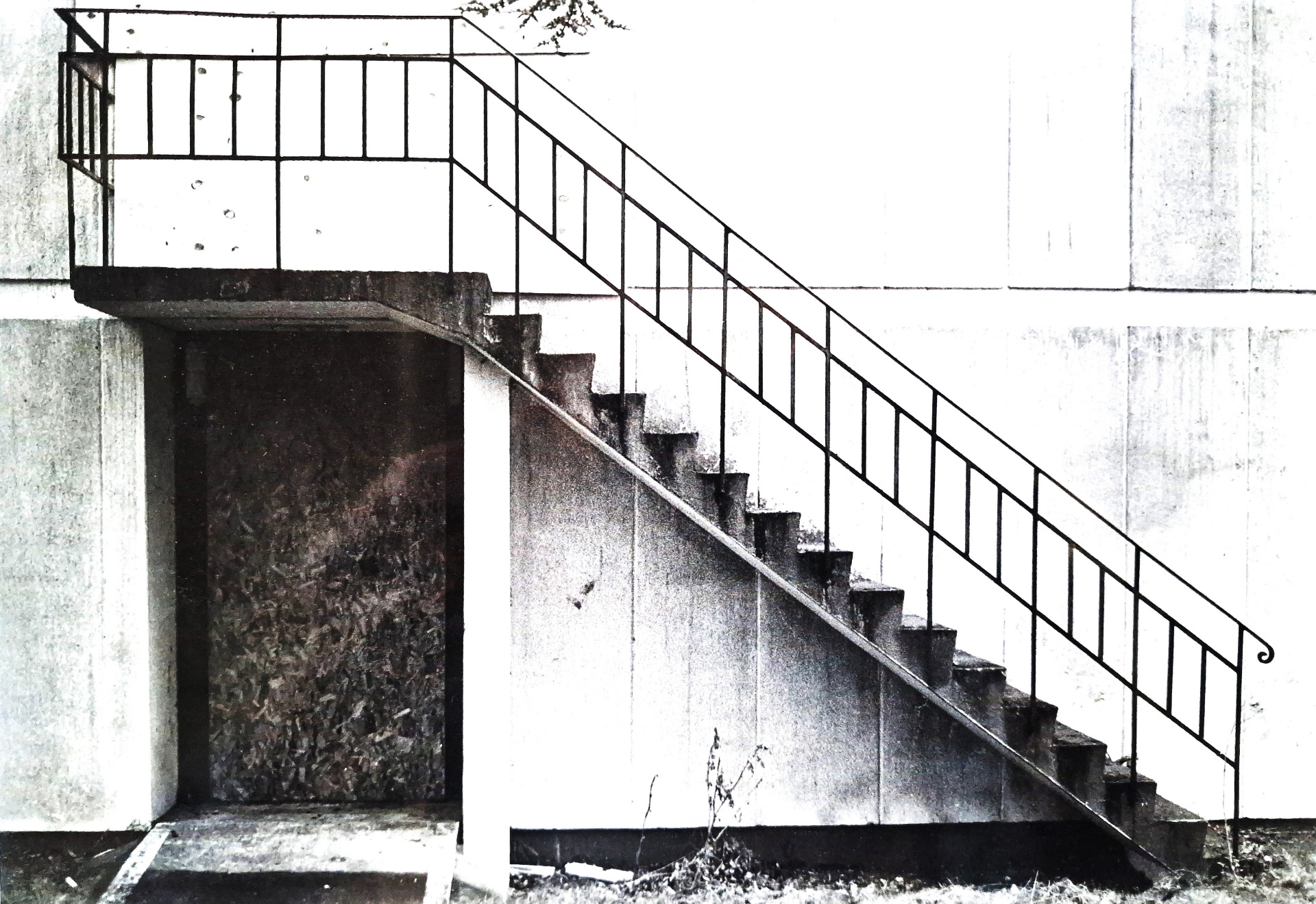 Black-and-white photograph of a concrete external staircase against a pale wall, empty and monumental.