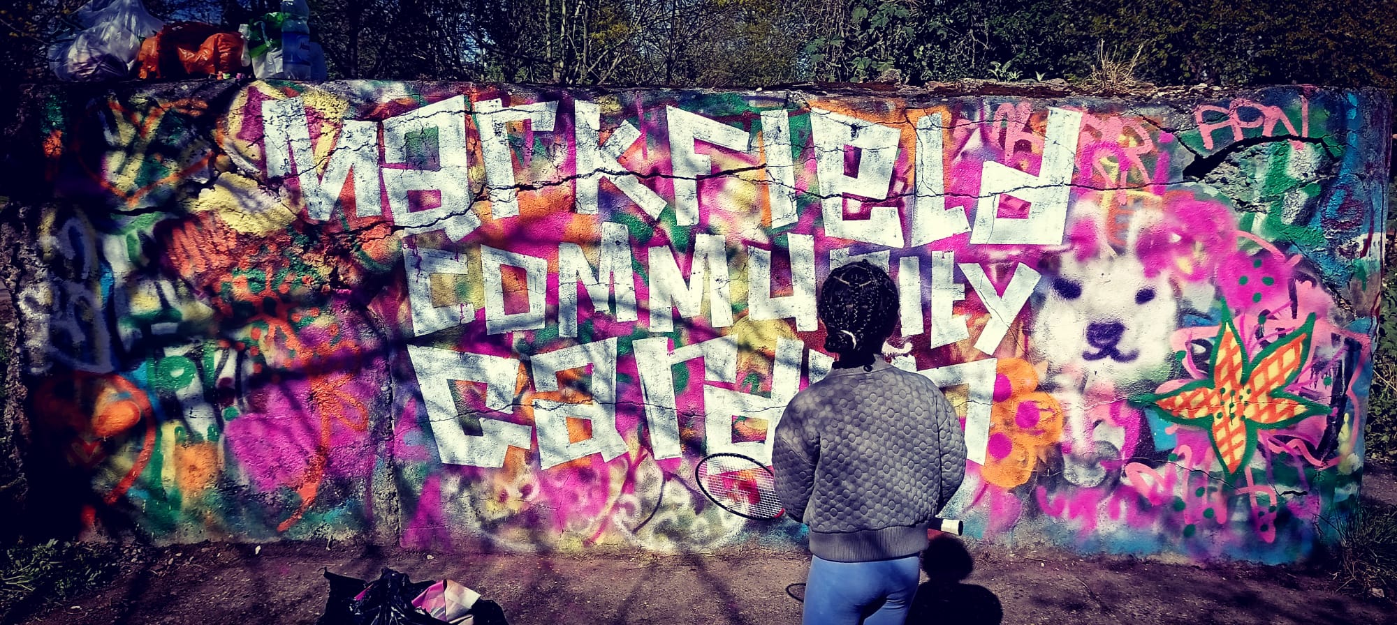 Kid painting 'Markfield Community Garden' letters on a graffiti wall.