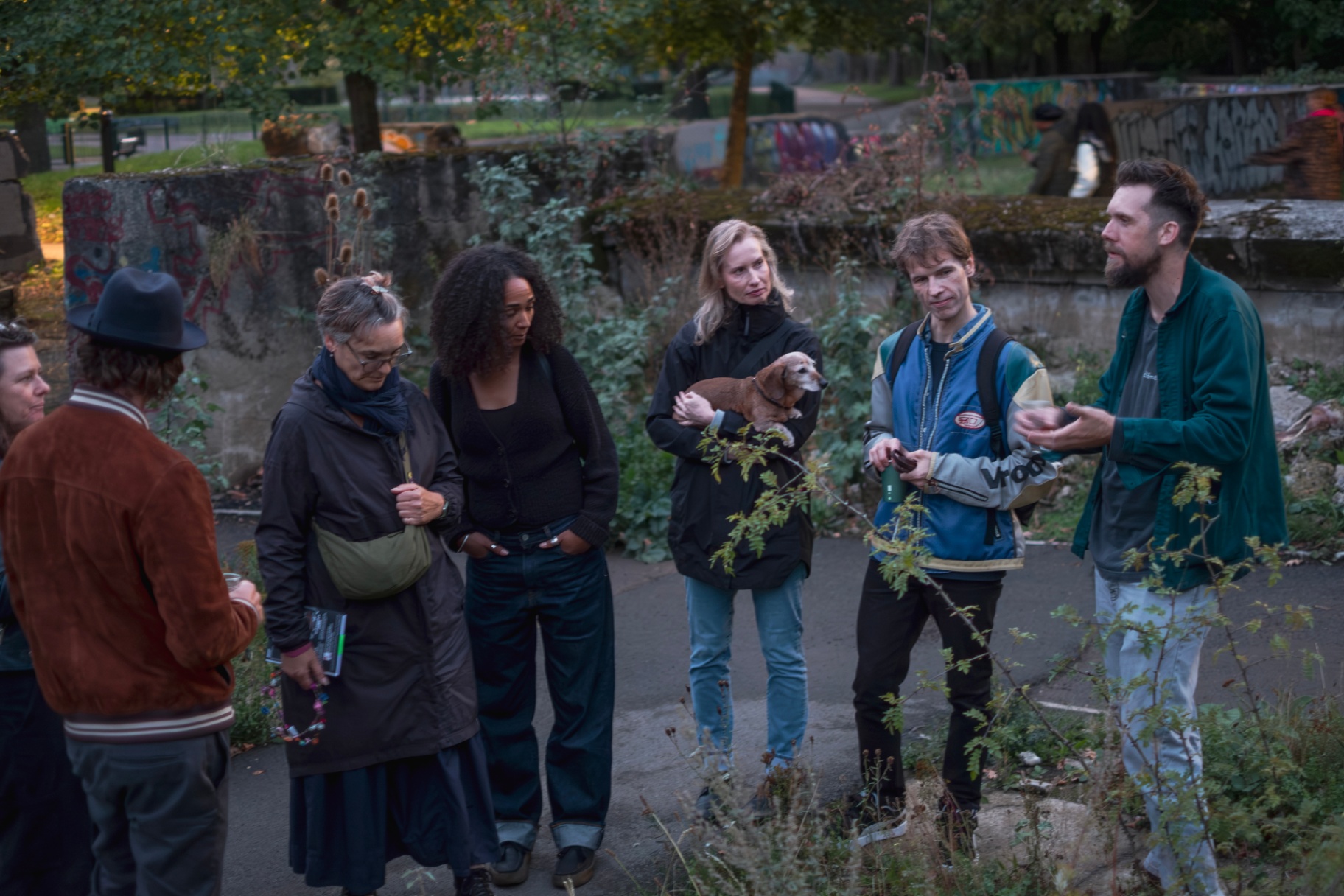 Small group on a garden tour at dusk, gathered among the concrete and planting.
